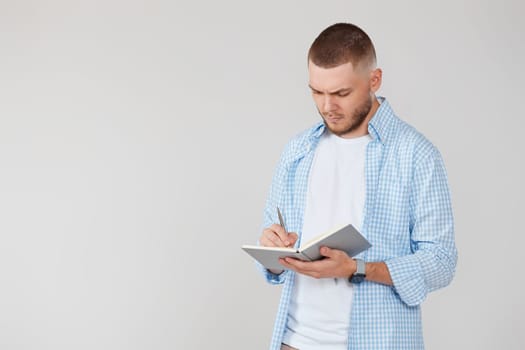 confident handsome man in casual blue shirt writing note in notebook. space for text
