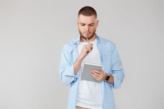 serious handsome man in casual blue shirt holding notebook, planning or thinking about question