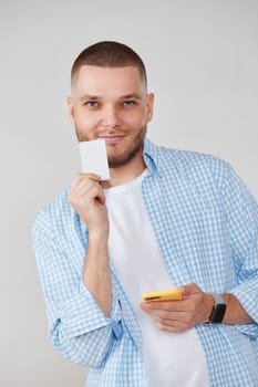 smiling handsome man with mobile cell phone and credit bank card making purchases by app. E-commerce concept