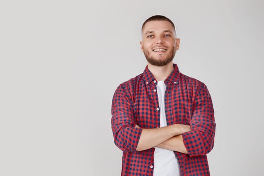 smiling young guy posing with crossed arms on gray studio background