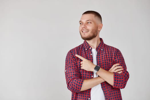 Young smiling handsome bearded man pointing to the side to present a product isolated on gray background