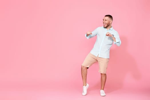 handsome smiling man in blue shirt dancing isolated on pastel pink background. Full length