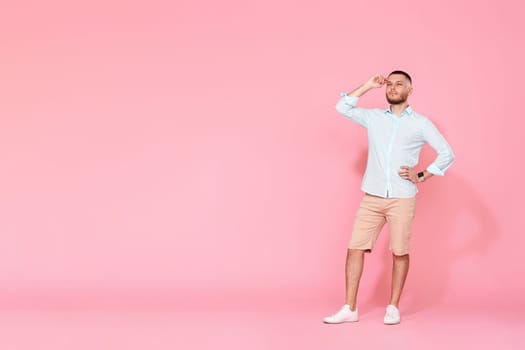positive dreamy thoughtful young man looking at the copy space and thinking isolated on pink background. Full length