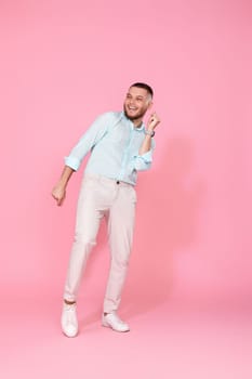 handsome smiling man in blue shirt dancing isolated on pastel pink background. Full length