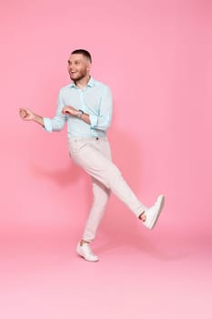 handsome smiling man in blue shirt dancing isolated on pastel pink background. Full length
