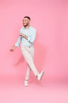 handsome smiling man in blue shirt dancing isolated on pastel pink background. Full length