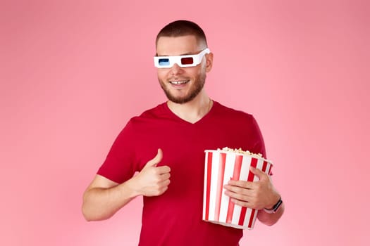 Young caucasian man eating popcorn and showing ok gesture on pink background