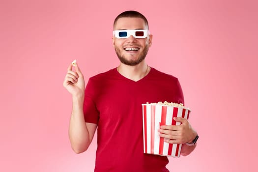 happy caucasian man in 3d glasses eating popcorn on pink background