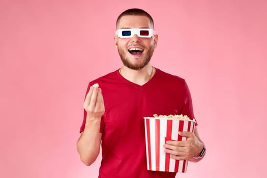 smiling caucasian man in 3d glasses eating popcorn on pink background
