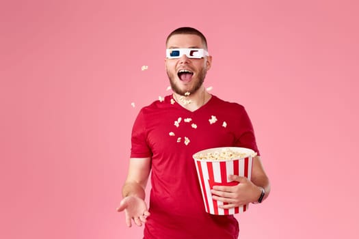 young happy man in 3d glasses throwing up and eating popcorn on pink background