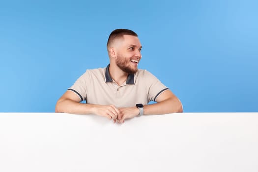 Portrait of cheerful man leaning on board with empty copy space isolated on blue background