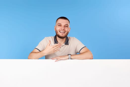 Portrait of friendly man in casual t-shirt with board with empty copy space isolated on blue background
