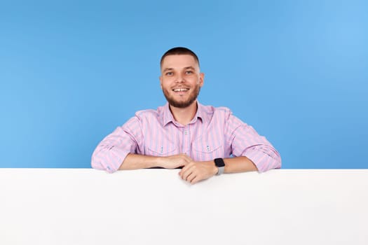 Portrait of cheerful man leaning on board with empty copy space isolated on blue background