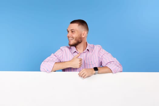 friendly man holding board with empty copy space and showing thumb up isolated on blue background
