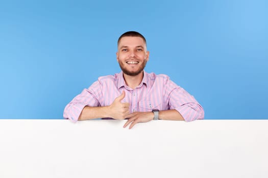 Portrait of cheerful bearded man holding board with empty copy space and showing thumb up isolated on blue background