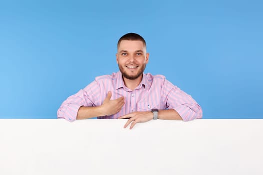 smiling man pointing at himself and placard with empty copy space isolated on blue background