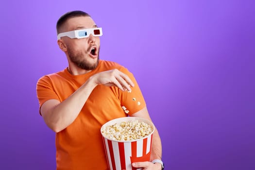 Shocked scared young man eating popcorn on purple background. copy space