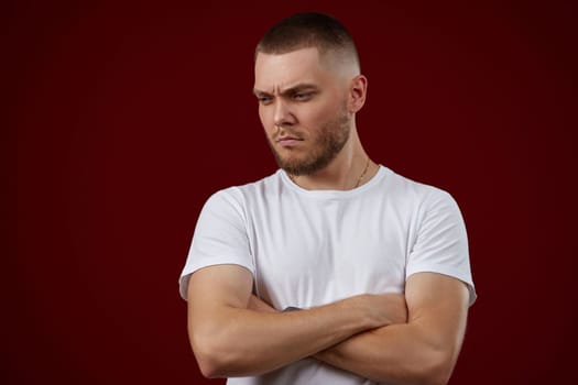 young handsome man in a white t-shirt thinks about something on a red background