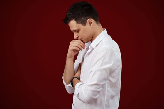 thoughtful man holding arms folded, touching chin with hand and looking down on red background