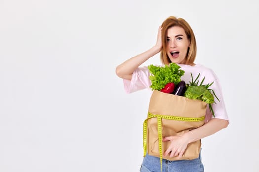 slim beautiful girl holds paper bag with vegetables and measuring tape isolated on white background. copy space. healthy food for diet