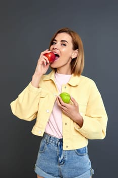 smiling blonde woman holding green and red apples on yellow background.