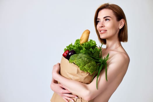 beautiful young woman holding paper bag with vegetables on gray background. healthy food. copy space.