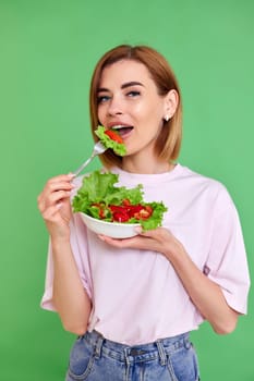 beautiful smiling blonde woman eating fresh vegetable salad on green background