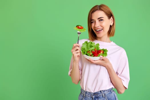 beautiful smiling healthy woman eating fresh vegetable salad, looking happy on green background