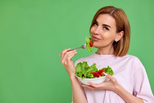 beautiful healthy woman eating fresh vegetable salad on green background. copy space