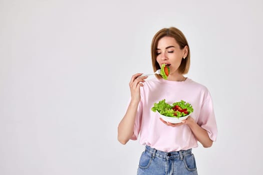 attractive caucasian girl eating fresh vegetable salad on white background. space for text