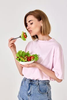 beautiful smiling blonde woman eating fresh vegetable salad on white background