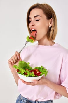 beautiful smiling blonde woman eating fresh vegetable salad on white background