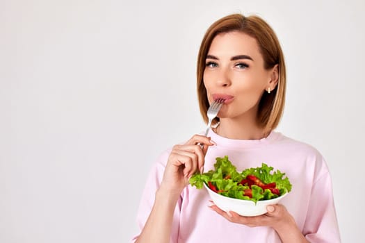 attractive caucasian woman eating fresh vegetable salad on white background