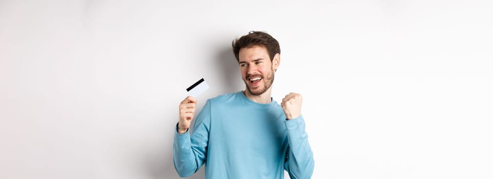 Happy man dancing with plastic credit card, smiling and saying yes, celebrating on white background. Copy space