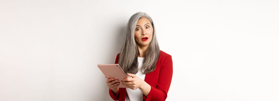 Business. Surprised asian businesswoman looking impressed after reading something on digital tablet, standing over white background.