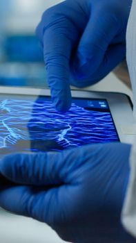 Close up of chemist doctor working on tablet with DNA scan image analysing treatment results. Scientist examining virus evolution using high tech researching vaccine development against covid19