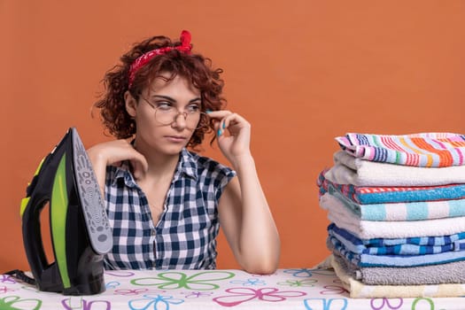A young woman with glasses and curly hair glances at the work being done. Ironing towels on an ironing board. Isolated from the background.