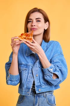 beautiful young woman holding with pleasure pizza slice on yellow background.