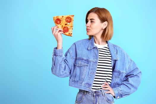 beautiful young woman with pizza slice on blue background. copy space
