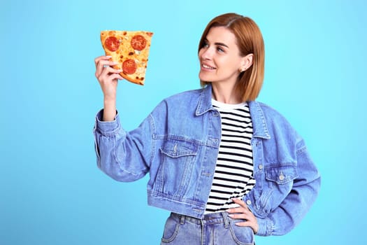 beautiful young woman with pizza slice on blue background. copy space