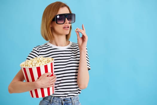 beautiful girl watching movie film, holding bucket of popcorn isolated on blue background. copy space