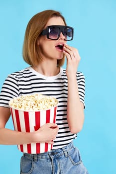beautiful girl watching movie filmand eating popcorn isolated on blue background