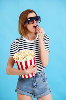 woman watching movie film, holding bucket of popcorn isolated on blue background