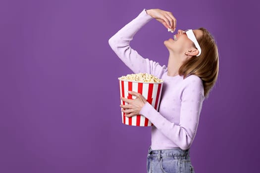 jouful caucasian woman in 3d glasses watching movie film, eating popcorn isolated on purple background