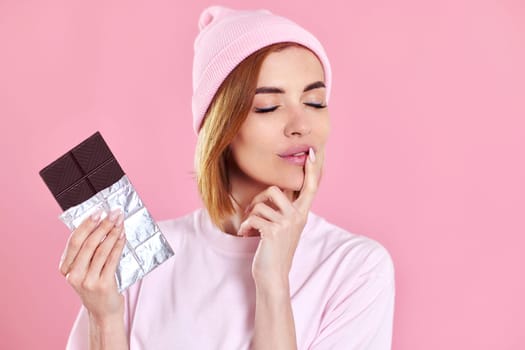 lovely beautiful woman enjoying dark chocolate isolated on pastel pink background