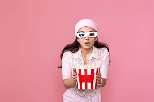 scared terrified woman watching movie film, holding bucket of popcorn on pink background