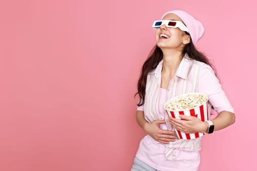 laughing woman watching comedy holding bucket of popcorn isolated on pink background