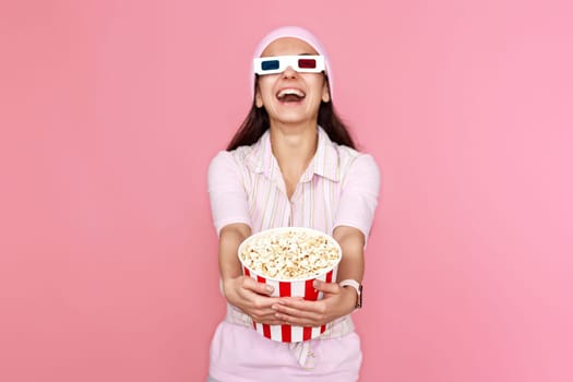 laughing woman watching comedy holding bucket of popcorn isolated on pink background. focus on popcorn