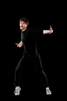 delighted young man in black t-shirt dancing on black background. Full length