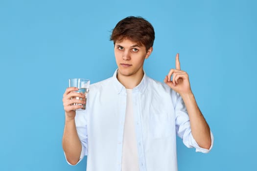 Young handsome man with drinking glass of water pointing up on blue background